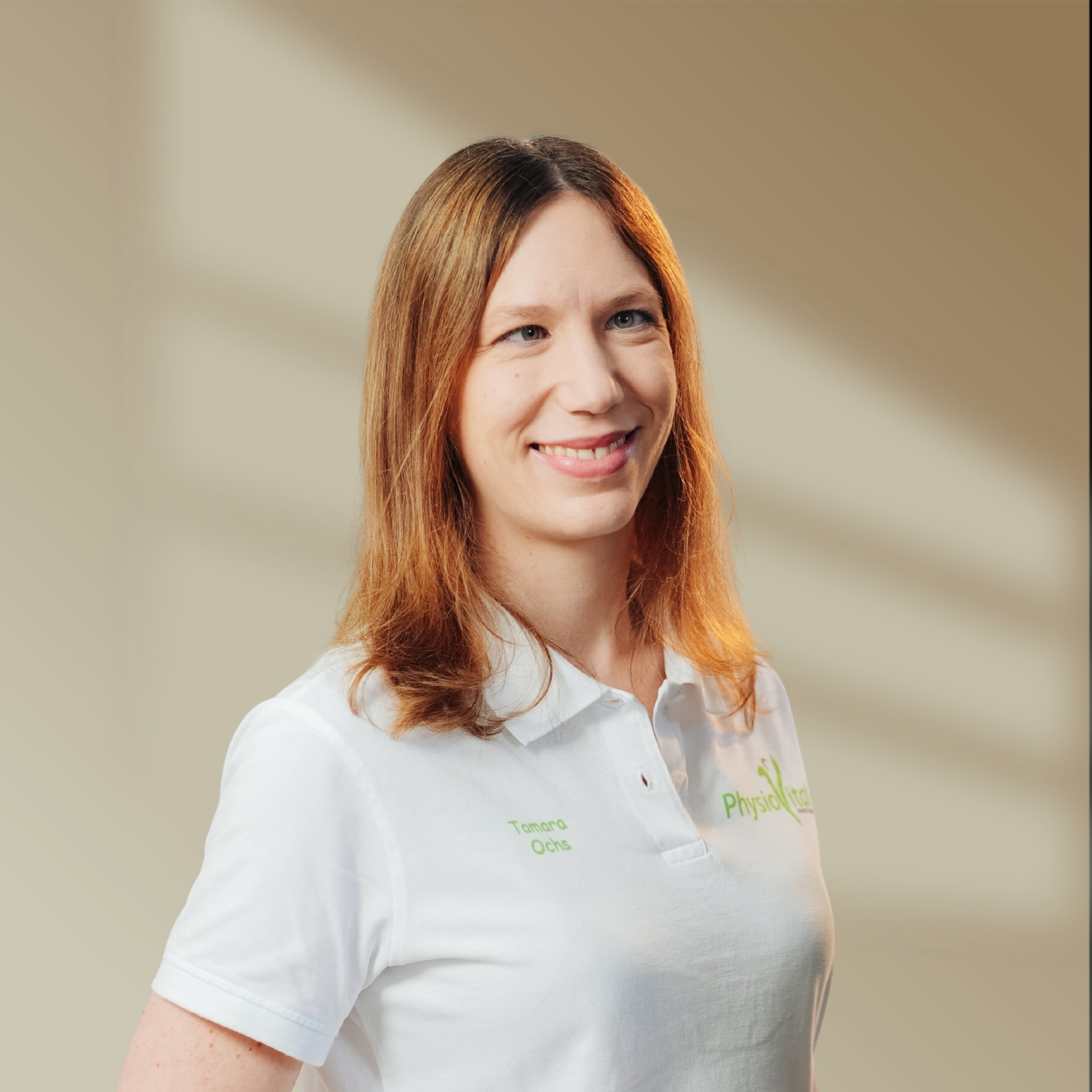 Frau mit schulterlangem braunen Haar und weißem Poloshirt lächelt; auf dem Shirt steht "Tamara" und "PhysioVital".